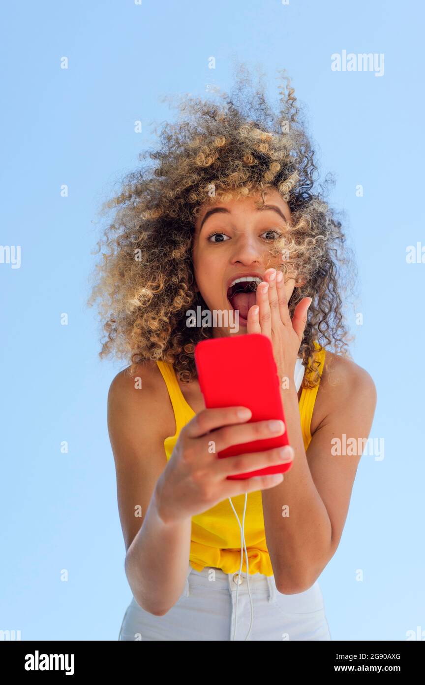 Surpris femme avec des cheveux bouclés à l'aide d'un téléphone portable Banque D'Images
