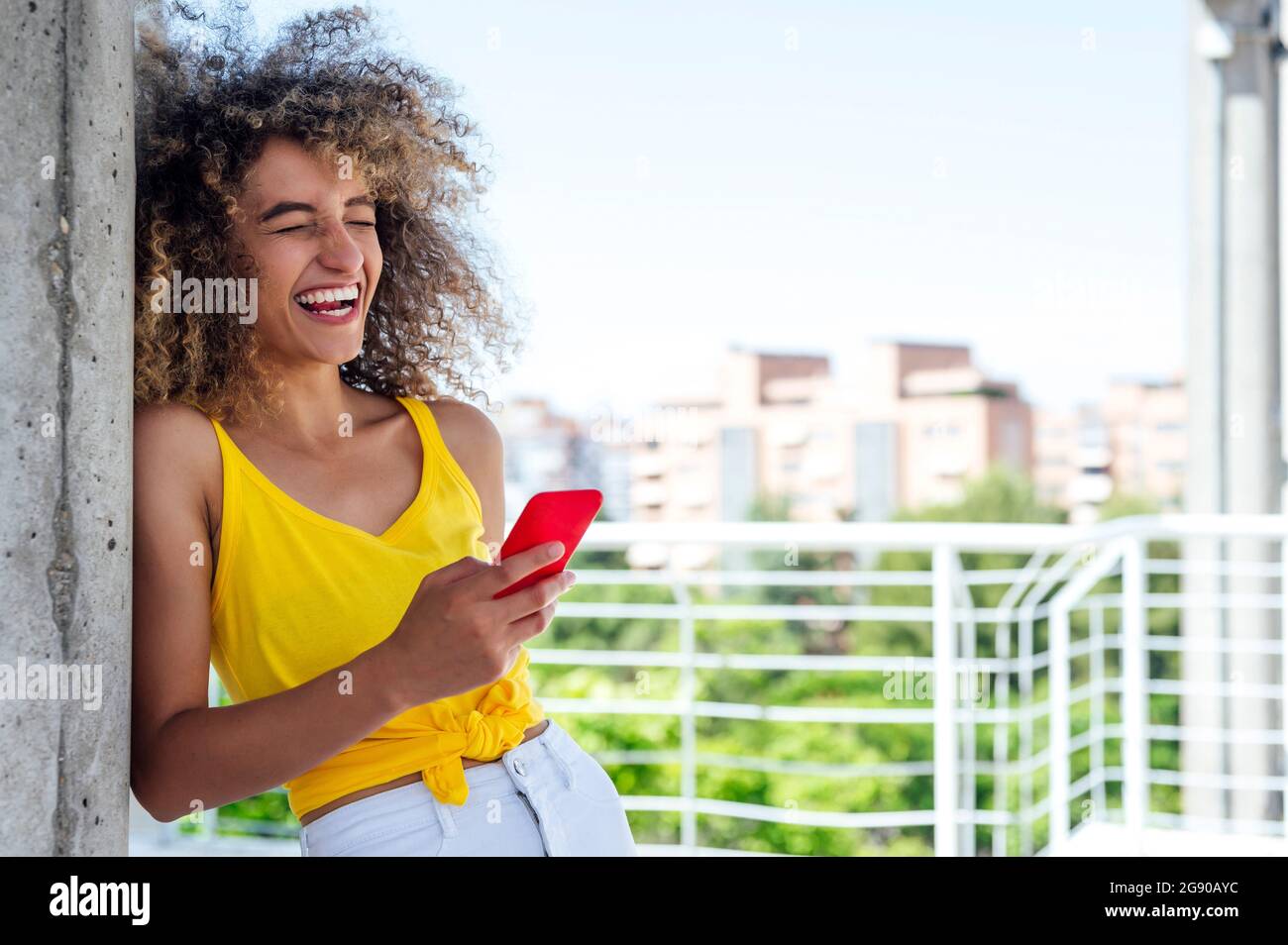 Une jeune femme riant avec les yeux fermés tout en utilisant un smartphone Banque D'Images