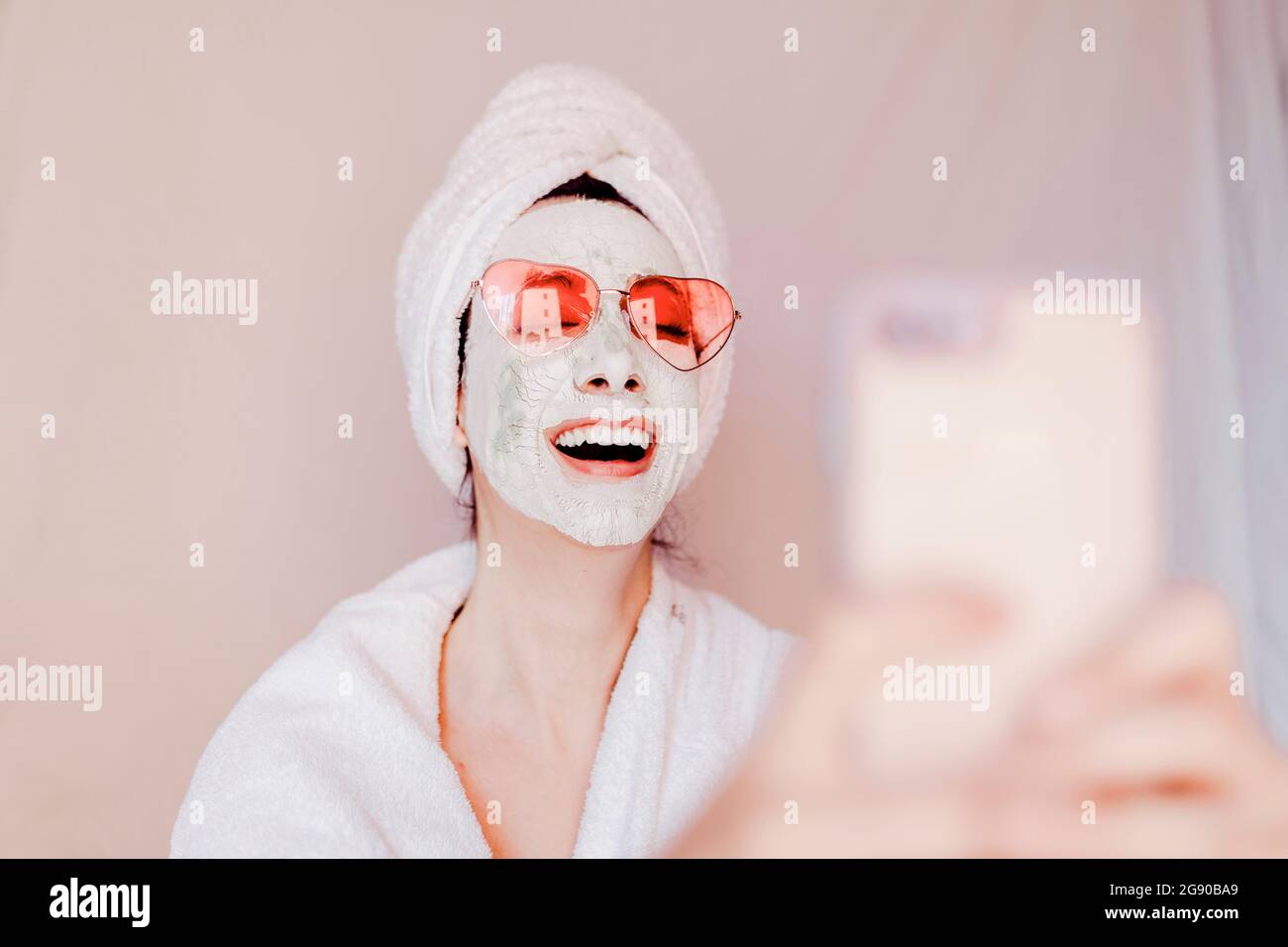 Bonne jeune femme avec masque de beauté prenant le selfie à travers le téléphone intelligent Banque D'Images