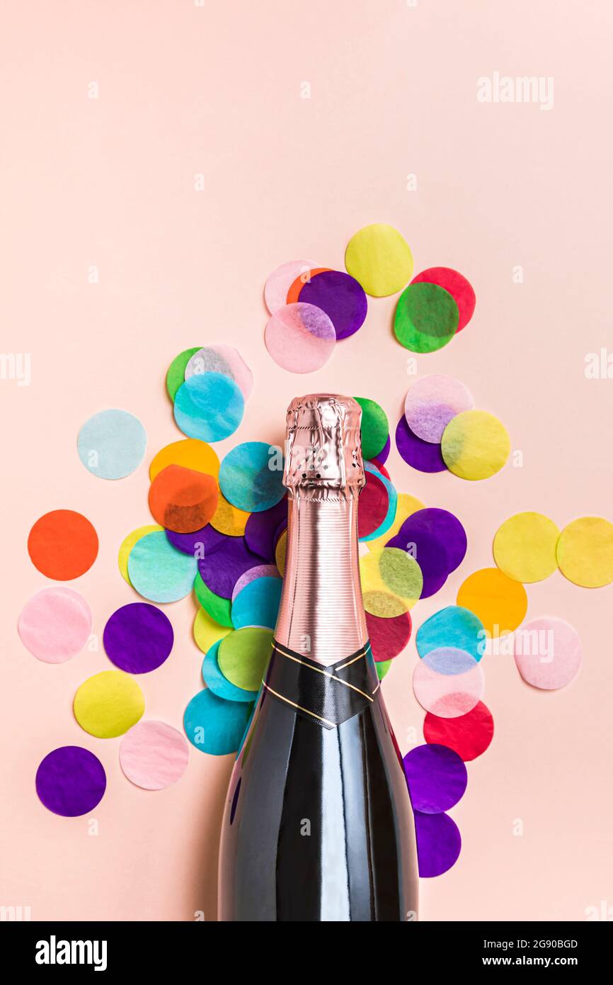 Studio avec une bouteille de champagne et des confettis colorés sur fond rose pastel Banque D'Images