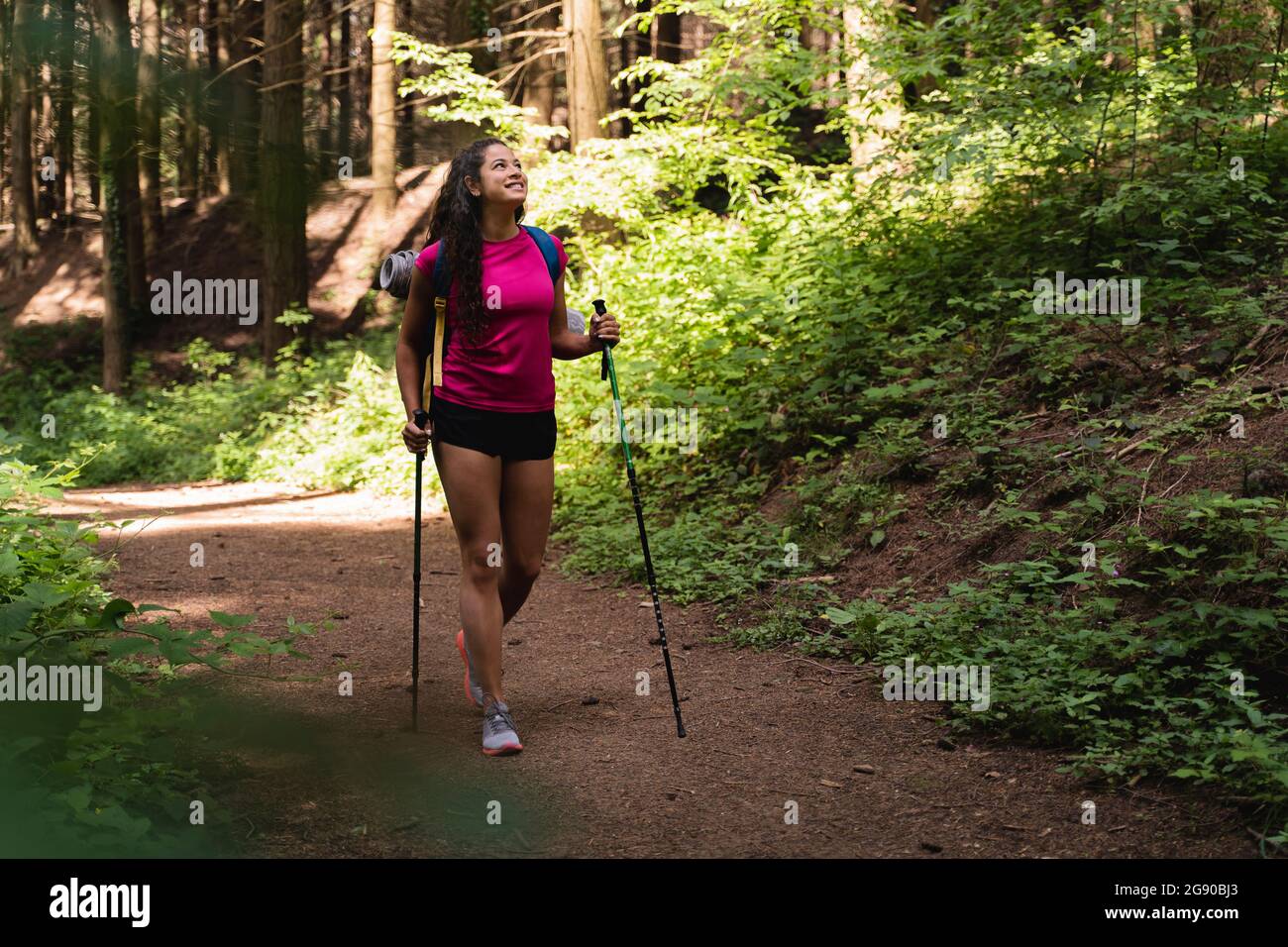 Jeune femme avec des bâtons de randonnée qui regardent loin en marchant dans la forêt Banque D'Images