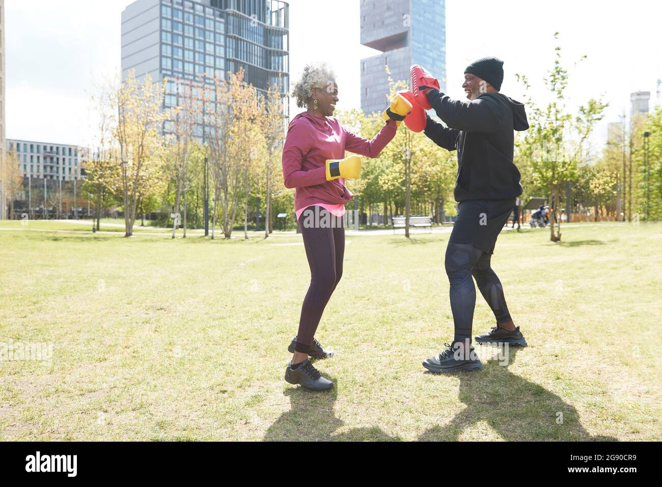 Femme souriante portant des gants pratiquant la boxe avec un homme au parc Banque D'Images