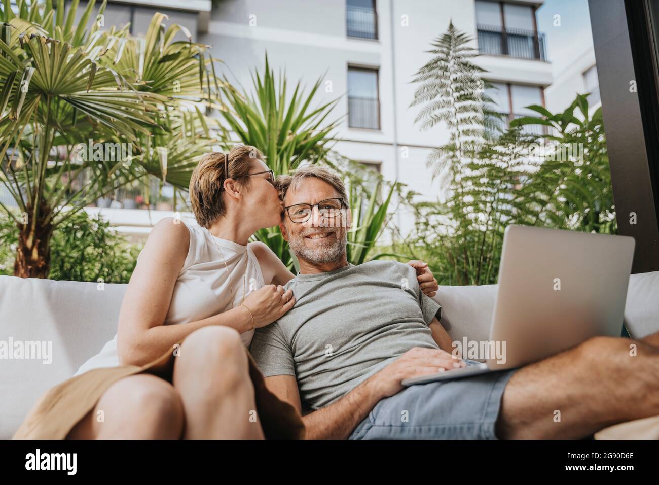 Femme embrassant homme assis avec un ordinateur portable sur le canapé sur la terrasse Banque D'Images
