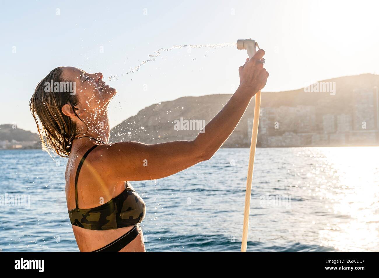 Femme avec les yeux fermés prenant la douche de tuyau de tuyau Banque D'Images