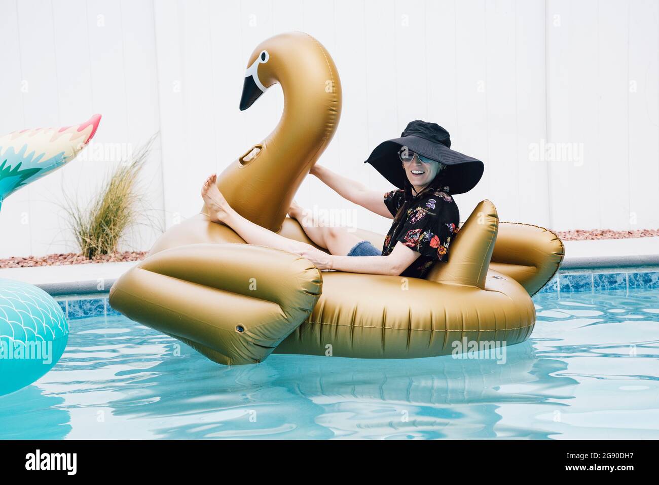 Femme souriante assise sur un cygne gonflable dans la piscine Banque D'Images