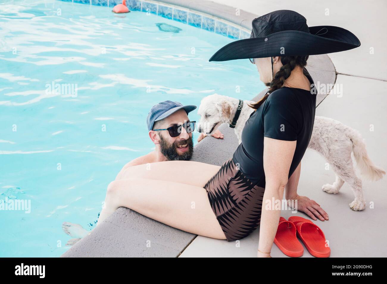 Homme barbu parlant avec une femme assise près de la piscine, près d'un chien dans le patio Banque D'Images