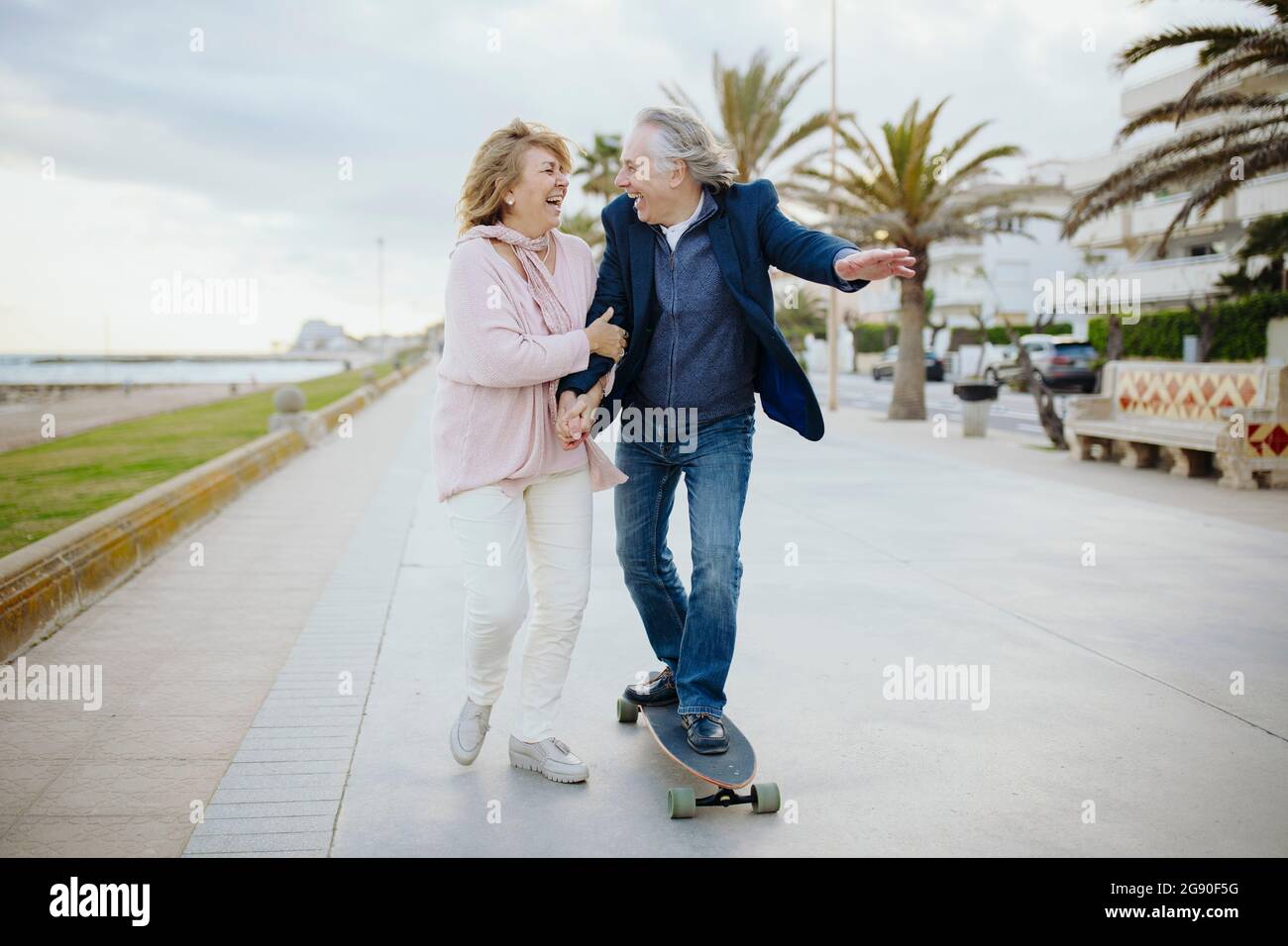 Joyeux homme mature skate par une femme marchant tout en tenant les mains sur la piste de marche Banque D'Images