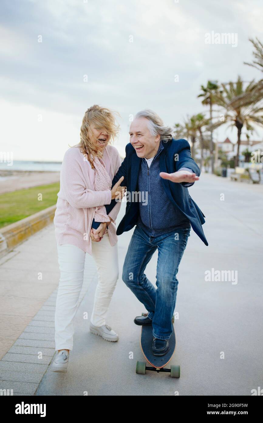 Homme mature qui apprécie le skateboard par une femme qui marche tout en tenant les mains Banque D'Images