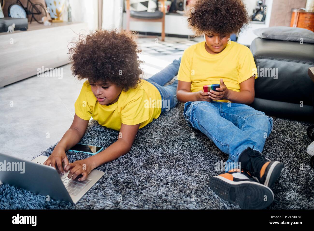 Afro garçon utilisant un ordinateur portable tandis que frère jumeau utilisant un smartphone à la maison Banque D'Images