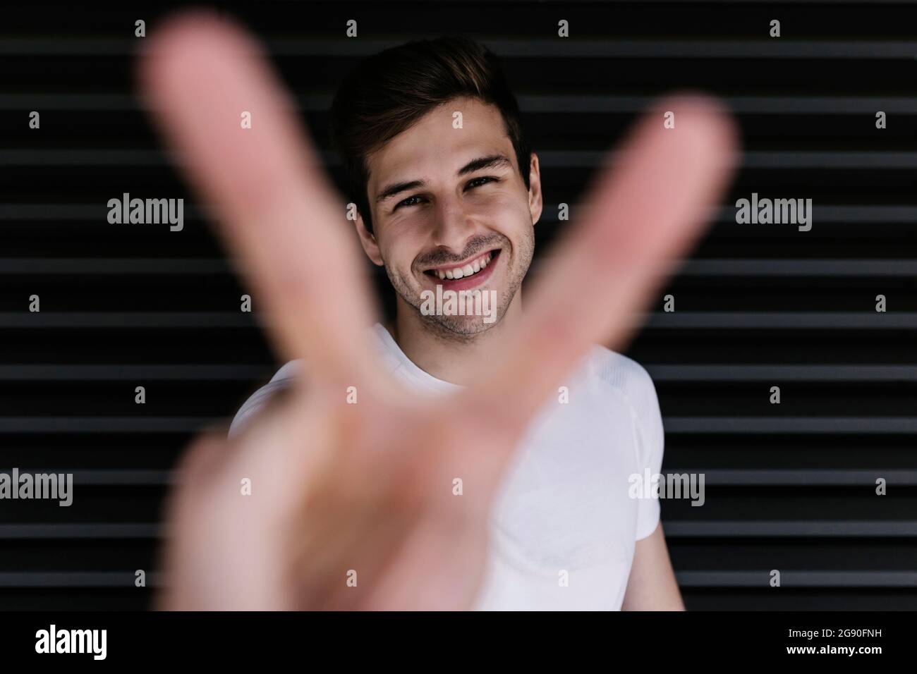 Jeune homme heureux montrant le geste de paix devant l'obturateur Banque D'Images