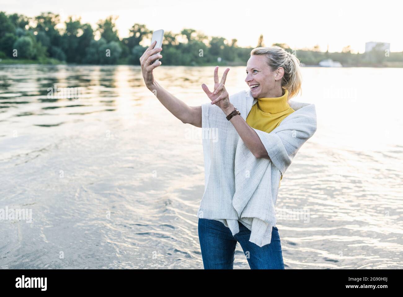 Une femme souriante signe la paix tout en prenant le selfie à travers le smartphone à la rive Banque D'Images