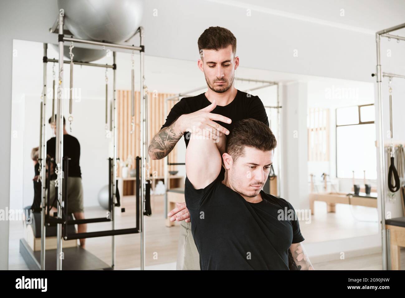 Instructeur de fitness masculin étirant le bras de l'homme tout en faisant de l'exercice dans le studio pilates Banque D'Images