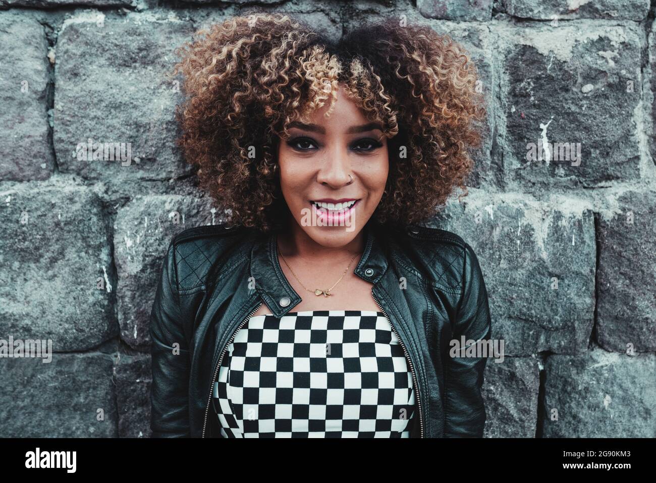 Femme de coiffure afro souriant devant le mur Banque D'Images Femme de coiffure afro souriant devant le mur Banque D'Images