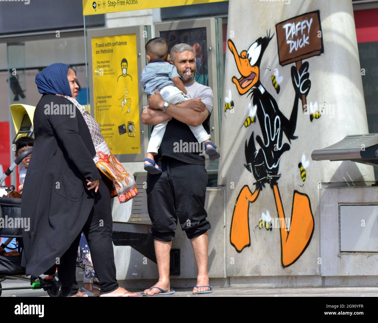 Un homme tient un bébé à côté d'une image du personnage de dessin animé Daffy Duck, qui fait partie d'un sentier d'art Looney Tunes qui a ouvert à Manchester, en Angleterre. Banque D'Images