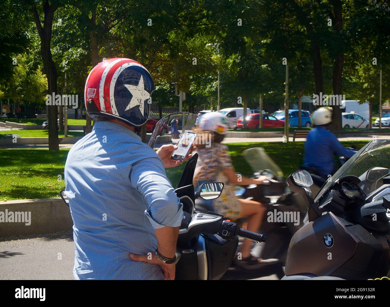 Un pilote d'un service de livraison consultant son téléphone mobile au milieu d'une rue avec le trafic de moto. Madrid, Espagne Banque D'Images