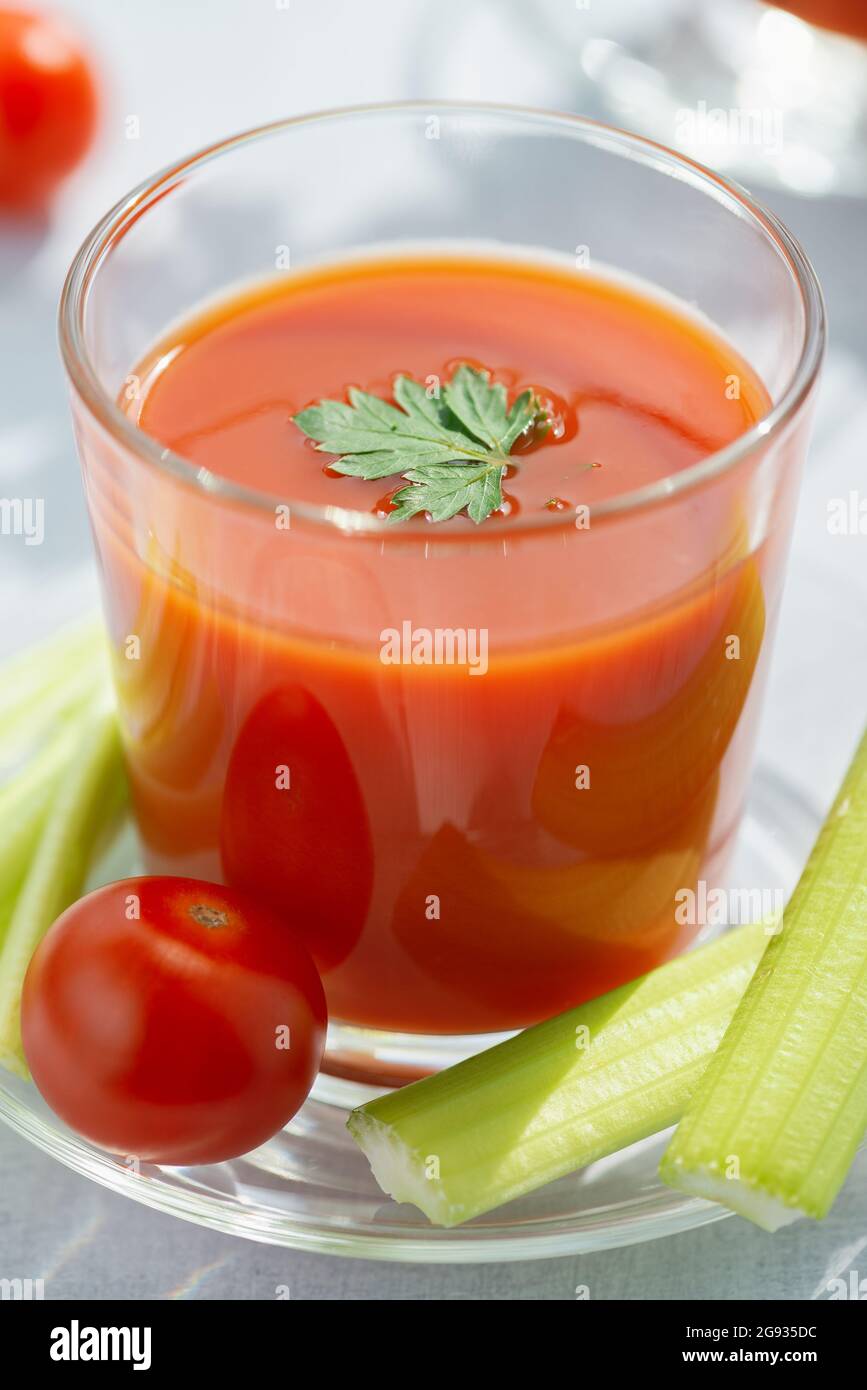 Un verre de jus de tomate frais, de céleri, de persil et de tomates mûres sur fond de bois clair Banque D'Images