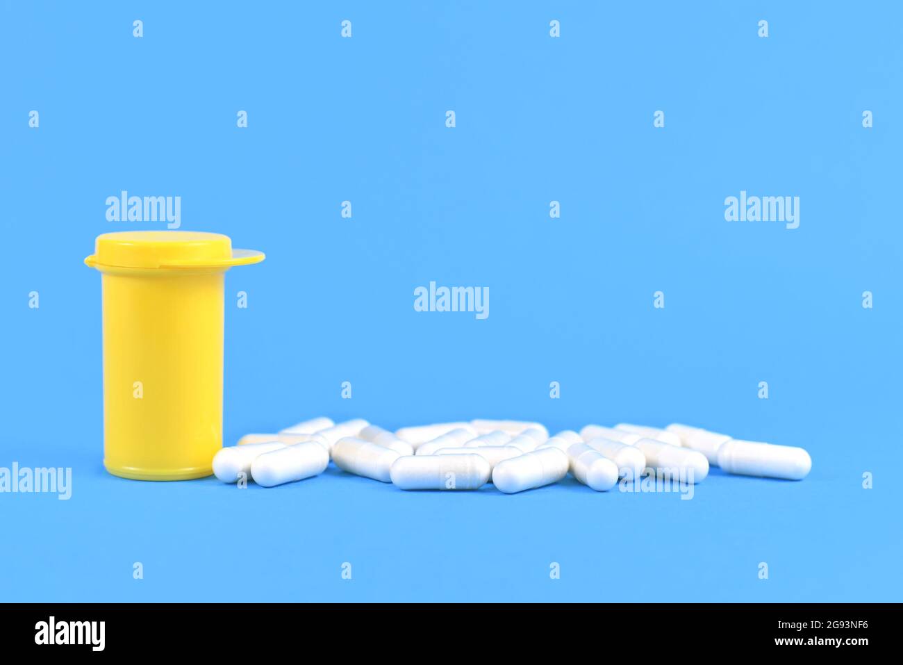 Capsules de pilules à côté du récipient de médecine jaune sur fond bleu clair Banque D'Images