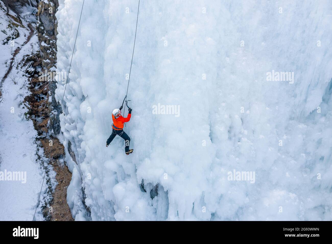 L'athlète masculin monte la falaise couverte de glace, balançant la hache de glace et en utilisant des crampons pour prendre un pied Banque D'Images
