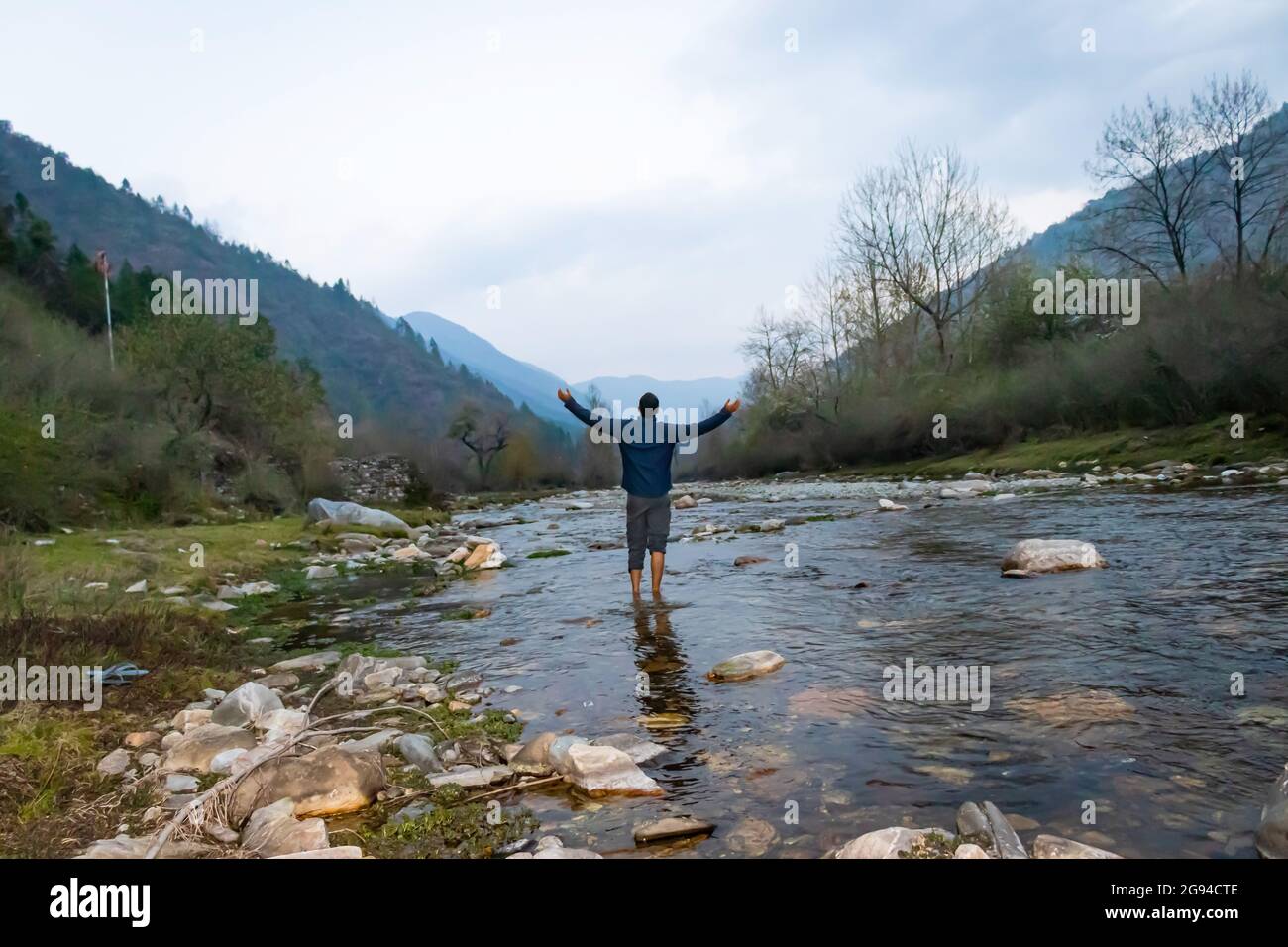 un jeune homme debout dans un cours d'eau avec vue sur la vallée de la montagne et les forêts le matin à partir d'un angle plat est pris à shergaon arunachal pradesh inde Banque D'Images