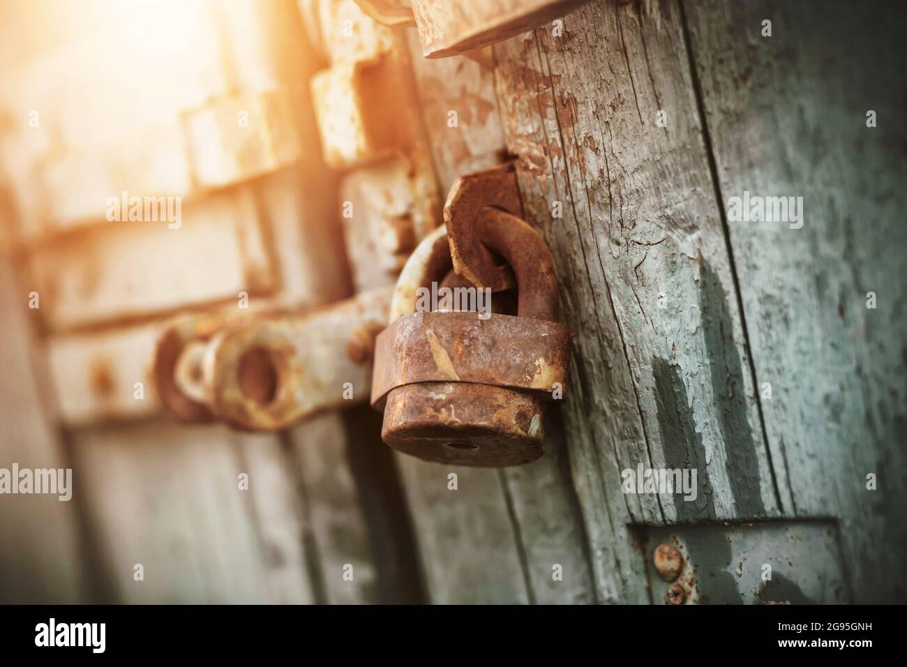 Un ancien cadenas rétro rouillé est suspendu sur une ancienne porte en bois, peinte avec de la peinture bleue, éclairée par la lumière du soleil. Le secret est derrière des portes fermées. Banque D'Images