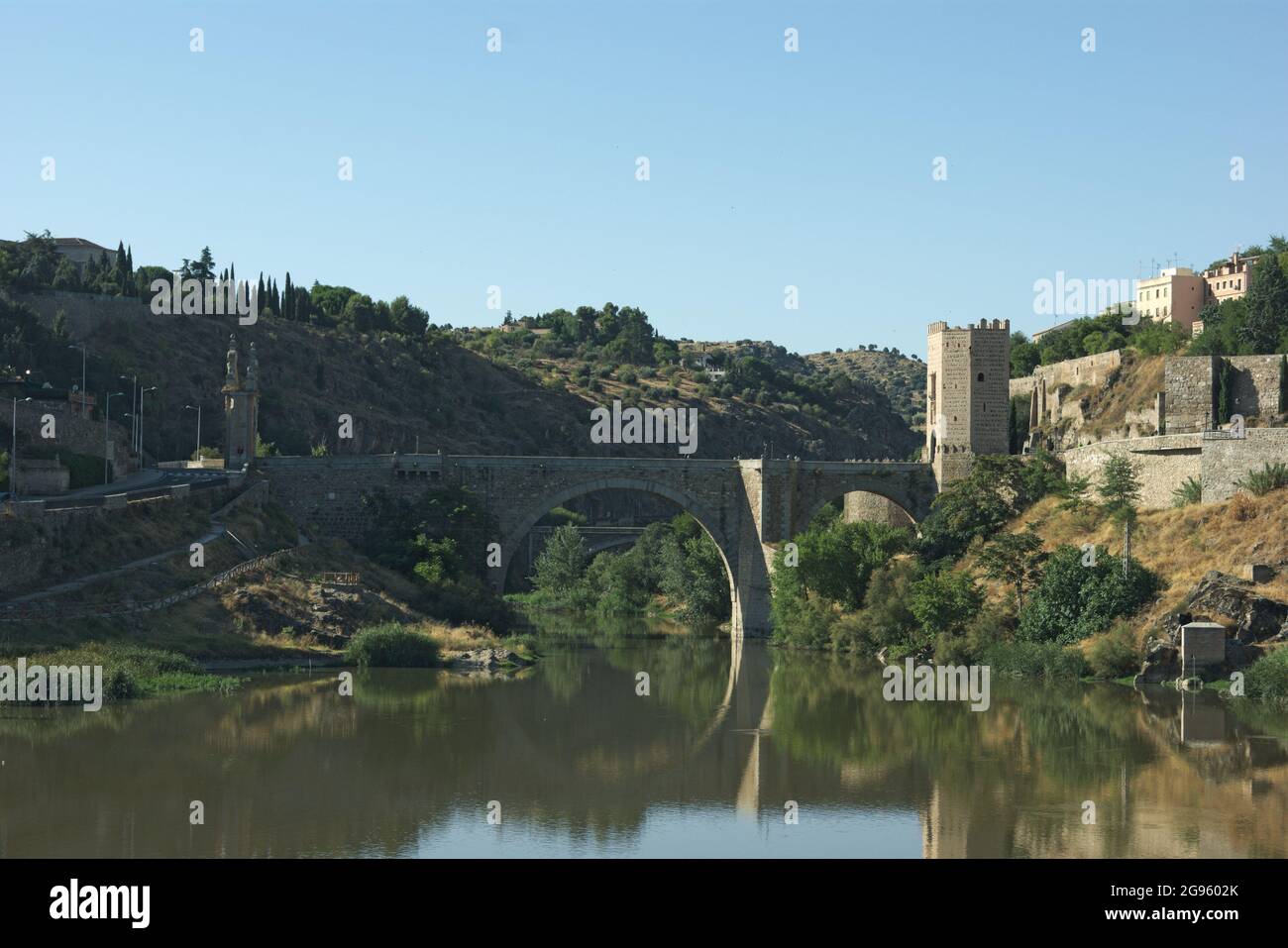 Vue sur le pont Alcantara à Tolède, Espagne. La forme élégante du pont se reflète sur les eaux fixes du Tage. Banque D'Images