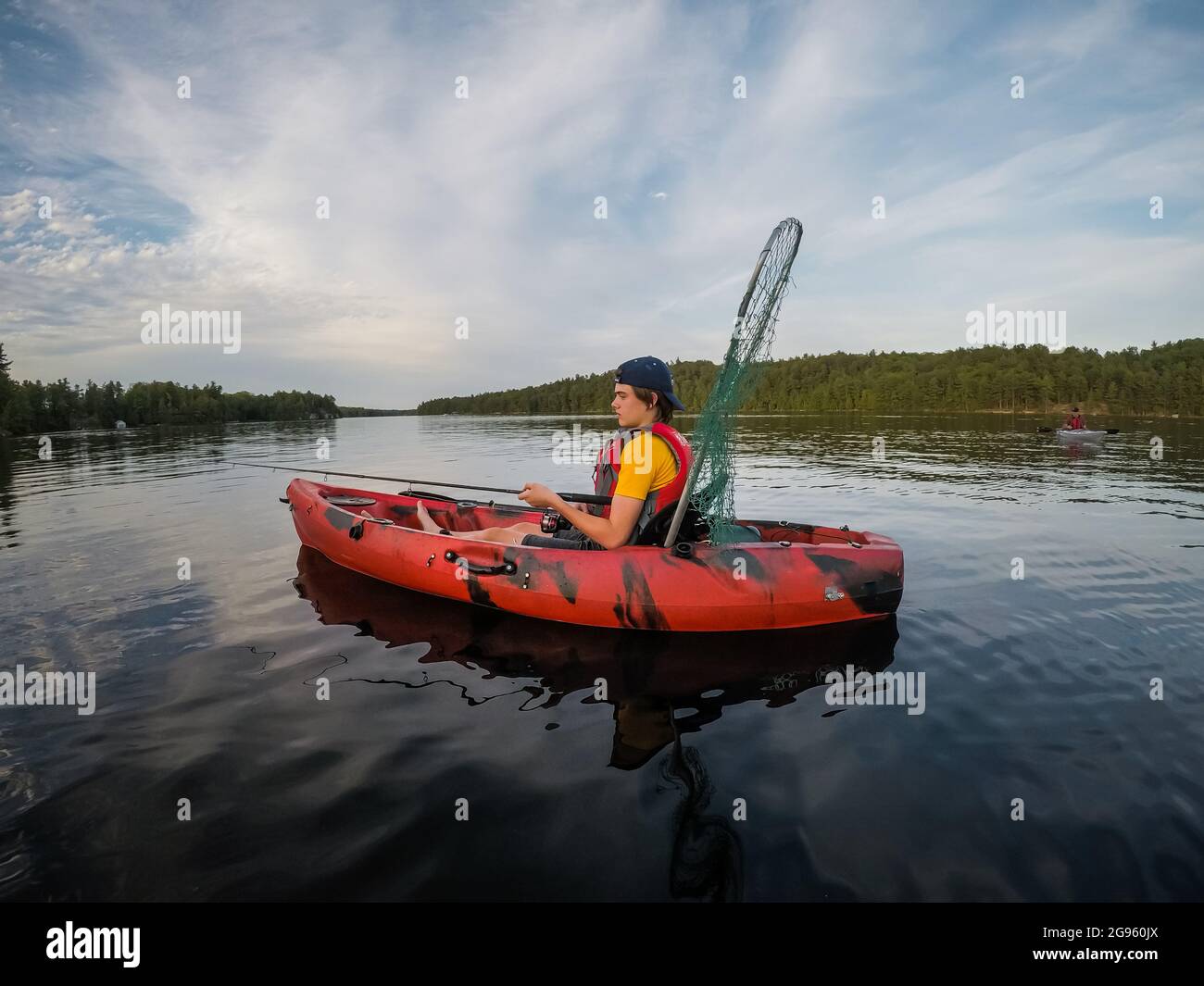 Un adolescent pêchant dans un kayak sur un lac par une journée d'été. Banque D'Images