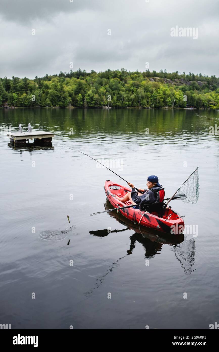 Un adolescent pêchant dans un kayak sur un lac par une journée d'été. Banque D'Images