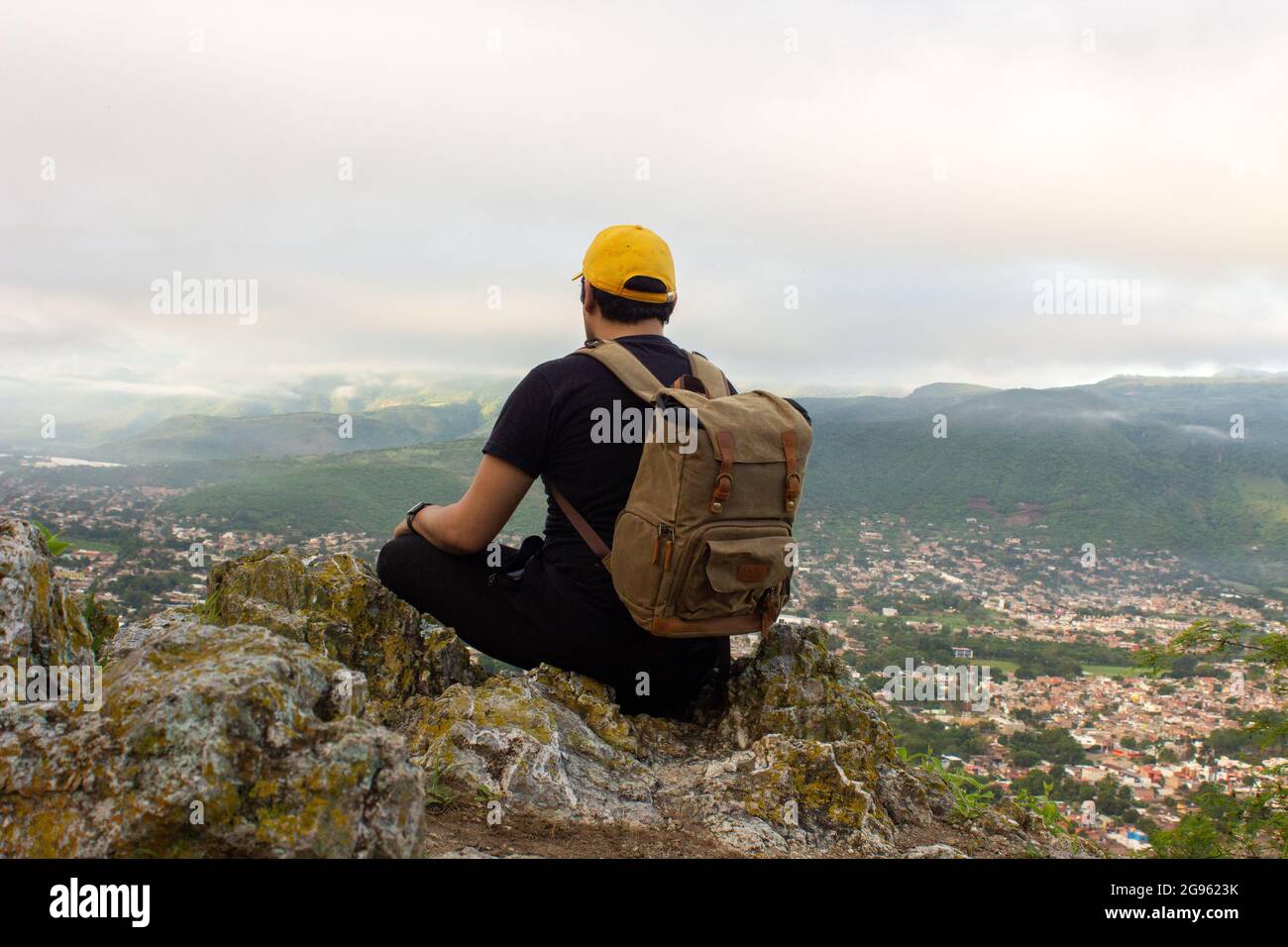 Un jeune randonneur mâle avec un sac à dos assis sur un rocher couvert de mousse au sommet d'une montagne Banque D'Images