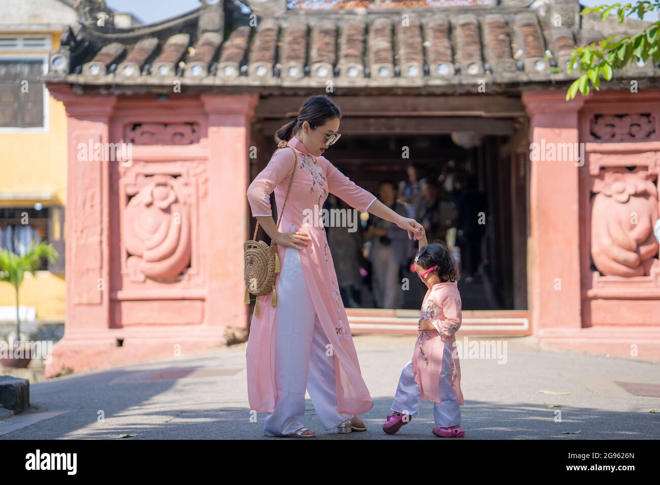 Jeune maman asiatique vêtue de vêtements similaires avec sa fille passant du temps avec elle pendant des vacances Banque D'Images