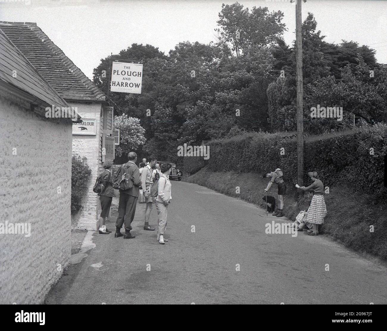 Années 1950, historique, un groupe de randonneurs ou de randonneurs dans les vêtements de l'époque et certains avec des sacs à dos en toile, debout dans une voie à l'extérieur du Plow and Harrow Pub à Litlington, Polegate, sur les South Downs, East Sussex, Angleterre, Royaume-Uni. Banque D'Images