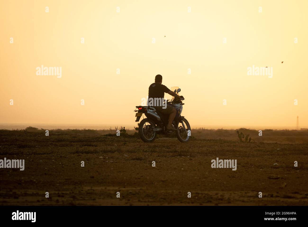 Uribia, la Guajira, Colombie - Mai 28 2021: L'homme latin de conduire une moto avec un fond jaune par les lumières du soleil de lever du soleil Banque D'Images