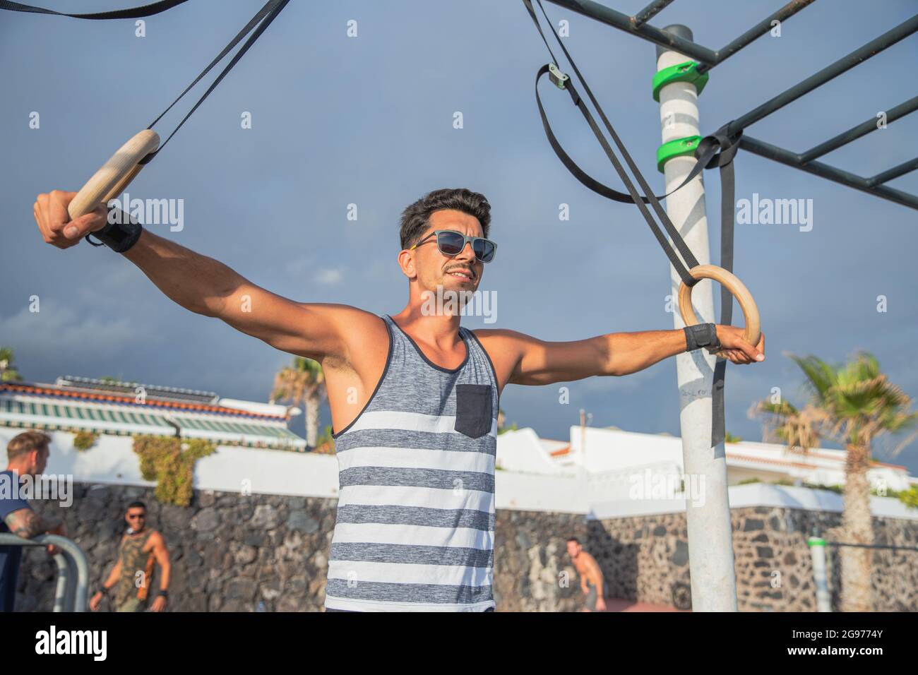 Les athlètes s'entraîne avec des anneaux dans une salle de sport en plein air. Homme avec des lunettes de soleil exécute l'entraînement des anneaux de gymnastique - concept de la personne sportive entraînement style de vie Banque D'Images