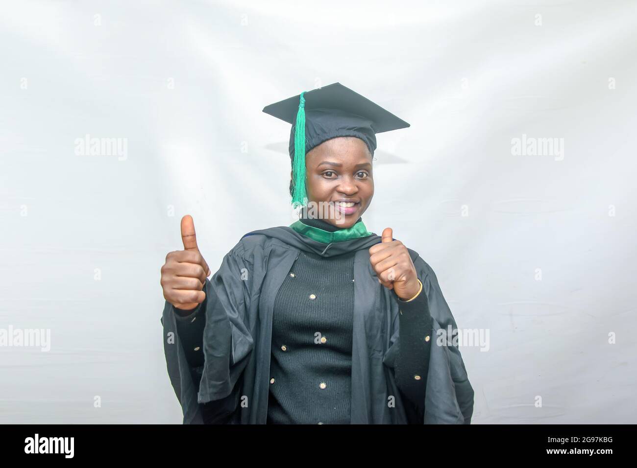 Photo d'une femme africaine finissant ou finissant ses études dans sa tenue de remise des diplômes noire et faisant joyeusement le pouce vers le haut geste Banque D'Images