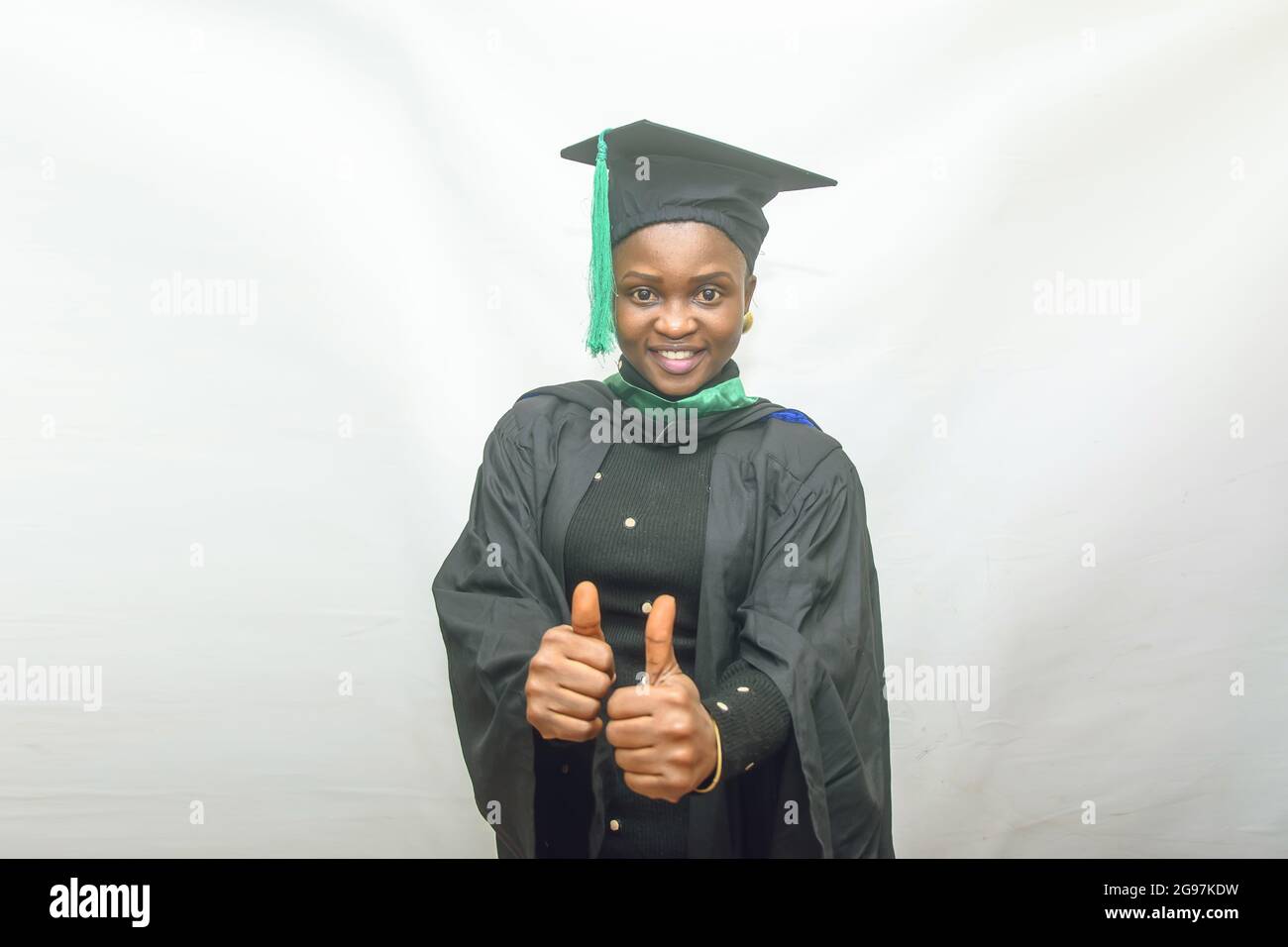 Photo d'une femme africaine finissant ou finissant ses études dans sa tenue de remise des diplômes noire et faisant joyeusement le pouce vers le haut geste Banque D'Images