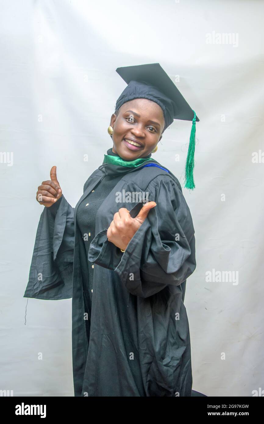 Photo d'une femme africaine finissant ou finissant ses études dans sa tenue de remise des diplômes noire et faisant joyeusement le pouce vers le haut geste Banque D'Images