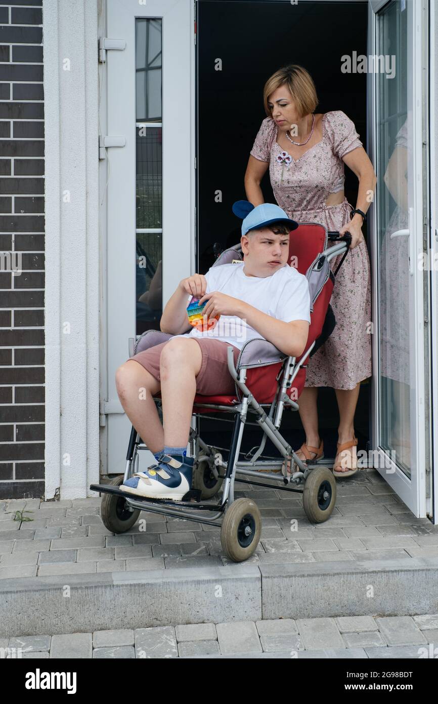 Mère avec enfant adolescent handicapé dans une grande poussette.  Accessibilité des personnes en fauteuil roulant. Femme passant par la  porte, personnes avec des besoins spéciaux Photo Stock - Alamy