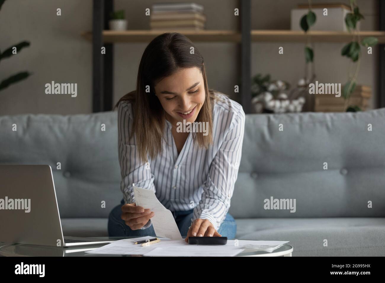 Une femme souriante gère ses finances personnelles effectue des calculs sur la calculatrice Banque D'Images