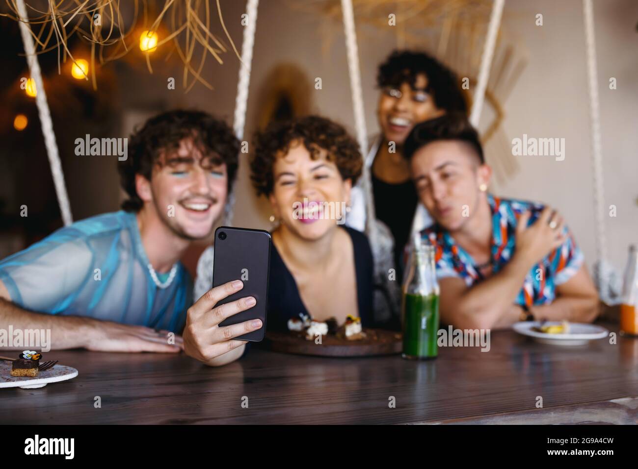 Groupe d'amis prenant un selfie ensemble dans un restaurant. Quatre jeunes reines sourient joyeusement tout en capturant le moment. Amis assis et Banque D'Images