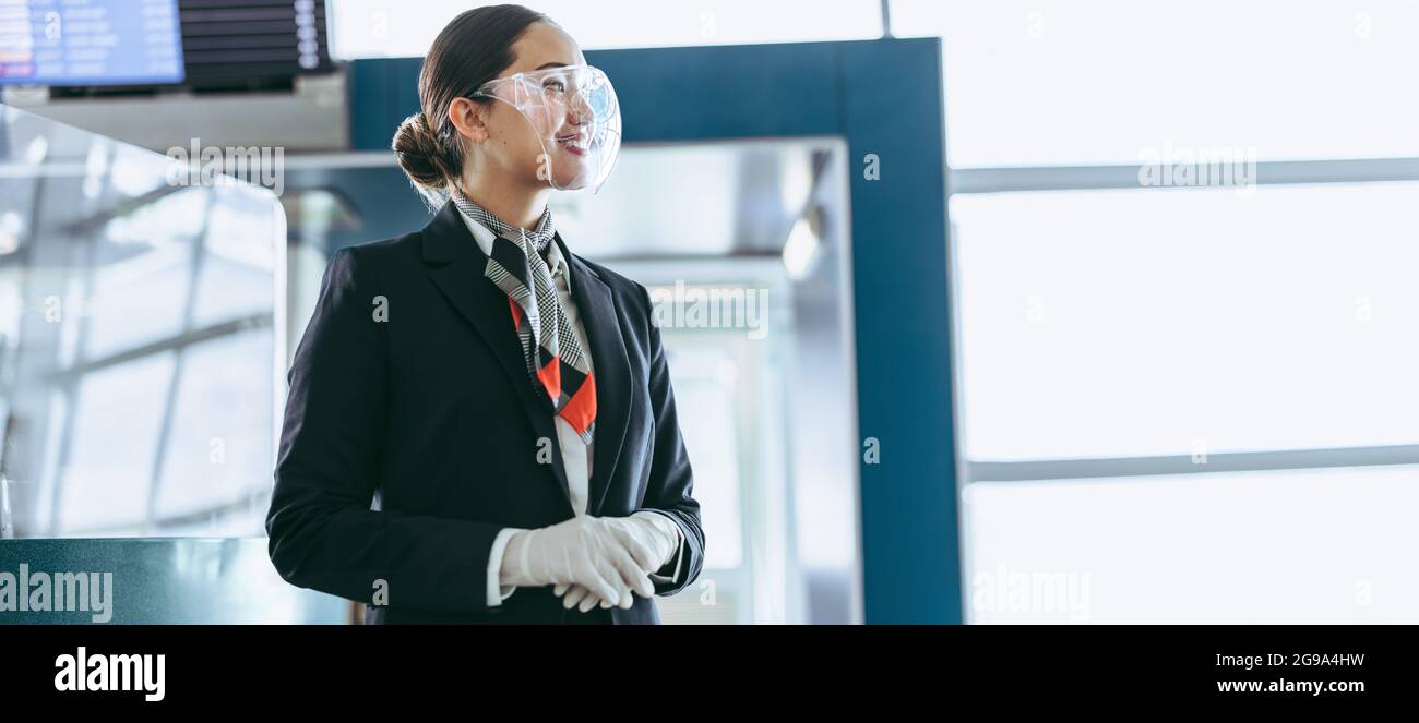 Vue latérale du personnel de la compagnie aérienne sur le panneau de protection situé à l'aéroport. Un employé de l'aéroport au terminal pendant une pandémie attend les touristes. Banque D'Images