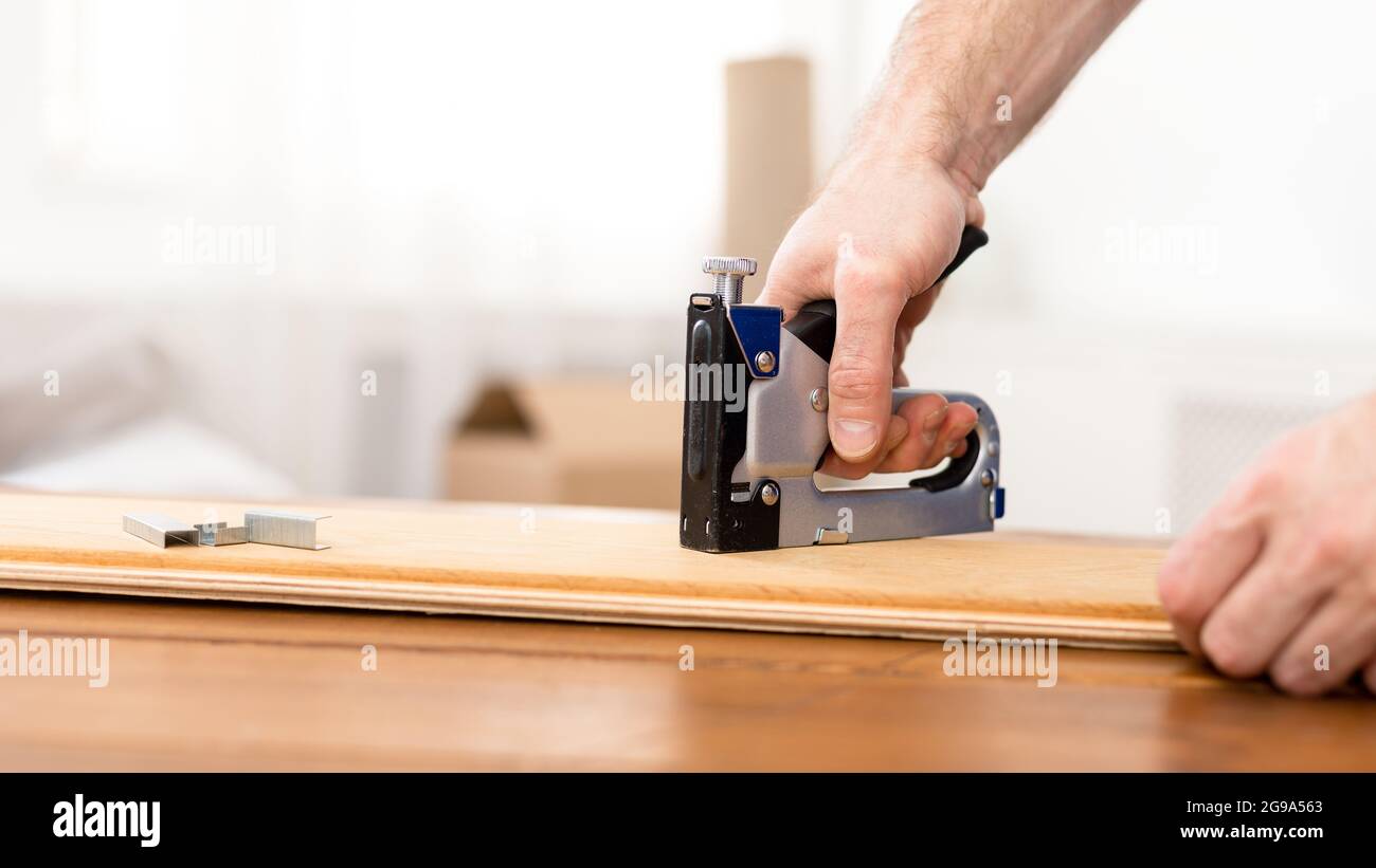 Charpentier méconnaissable utilisant un pistolet à agrafes pour faire des meubles à l'intérieur, Panorama Banque D'Images