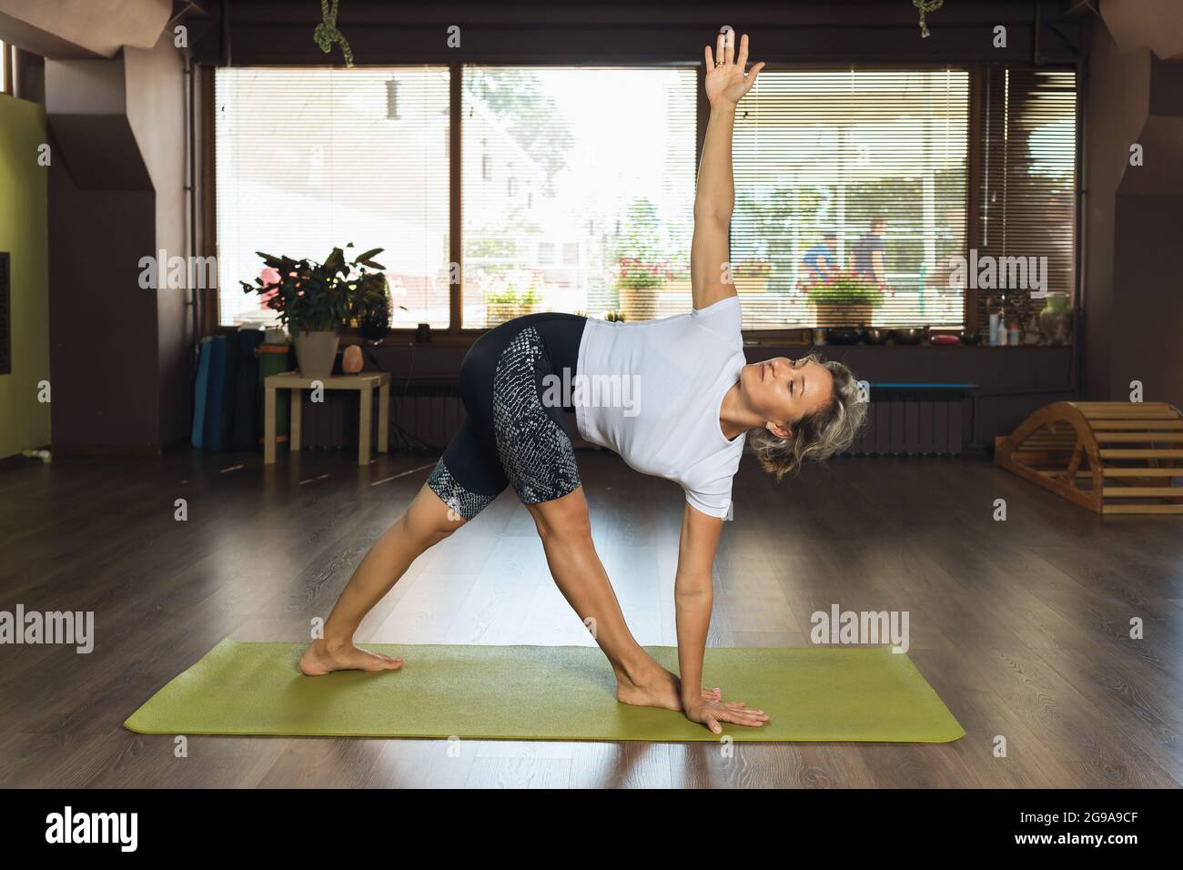 Une femme pratiquant le yoga, debout sur un tapis, exécute l'exercice utthita trikonasana, posture triangulaire dans le studio Banque D'Images
