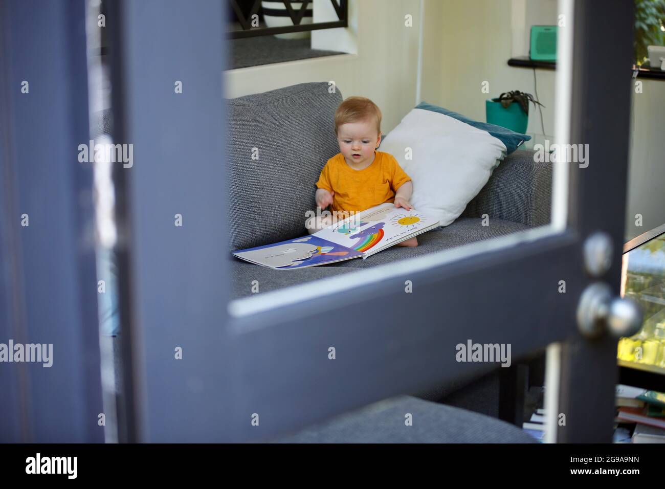 Un adorable enfant australien jouant avec un livre coloré sur un canapé dans une maison Banque D'Images
