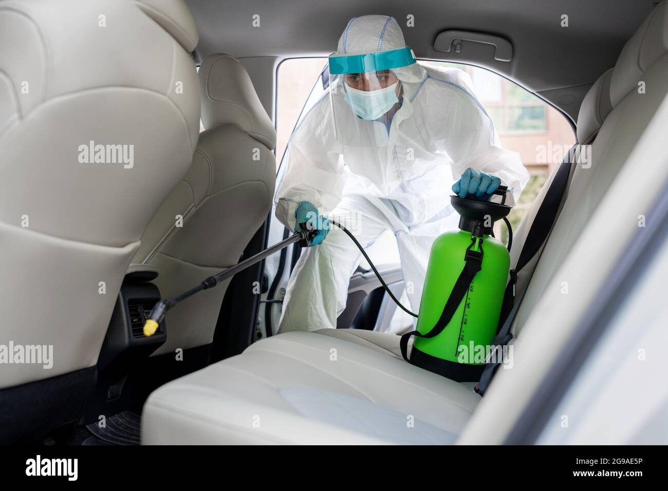 Homme en costume de noisette avec masque désinfectant à l'intérieur de la voiture, essuyer les surfaces qui sont fréquemment touchées Banque D'Images