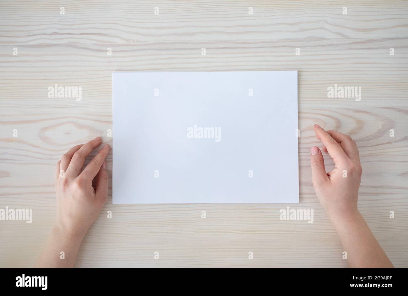 Mains de femmes avec feuille de papier blanc vierge sur fond de table en bois, vue de dessus, espace vide, plat Banque D'Images