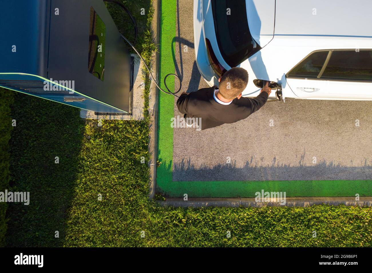 Vue d'oiseau d'un jeune homme du Caucase qui charge une voiture électrique blanche à une station de charge publique Banque D'Images