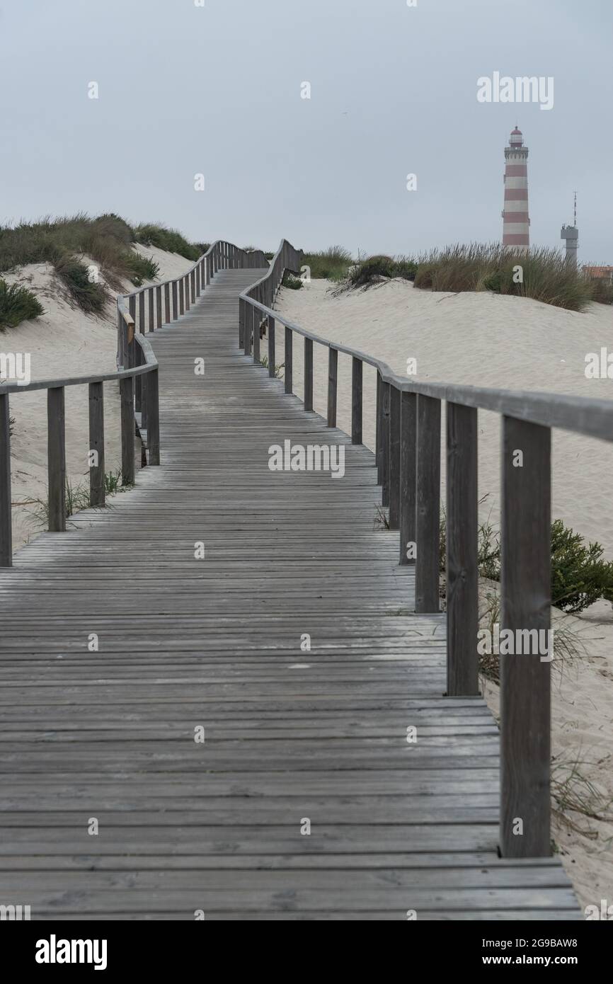 Passerelles en bois le long des dunes de la plage de Barra avec le phare d'Aveiro en arrière-plan en une journée nuageux. Portugal Banque D'Images