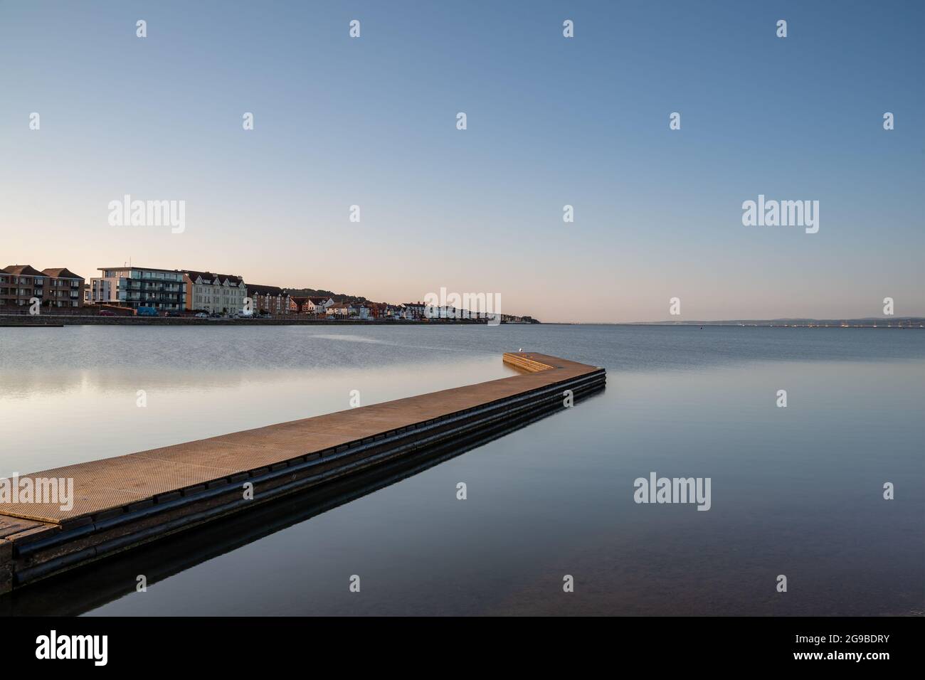 West Kirby, Wirral, Royaume-Uni. Ponton sur le lac marin pendant une matinée d'été calme. Les maisons le long de South Parade ligne le long de l'horizon. Banque D'Images