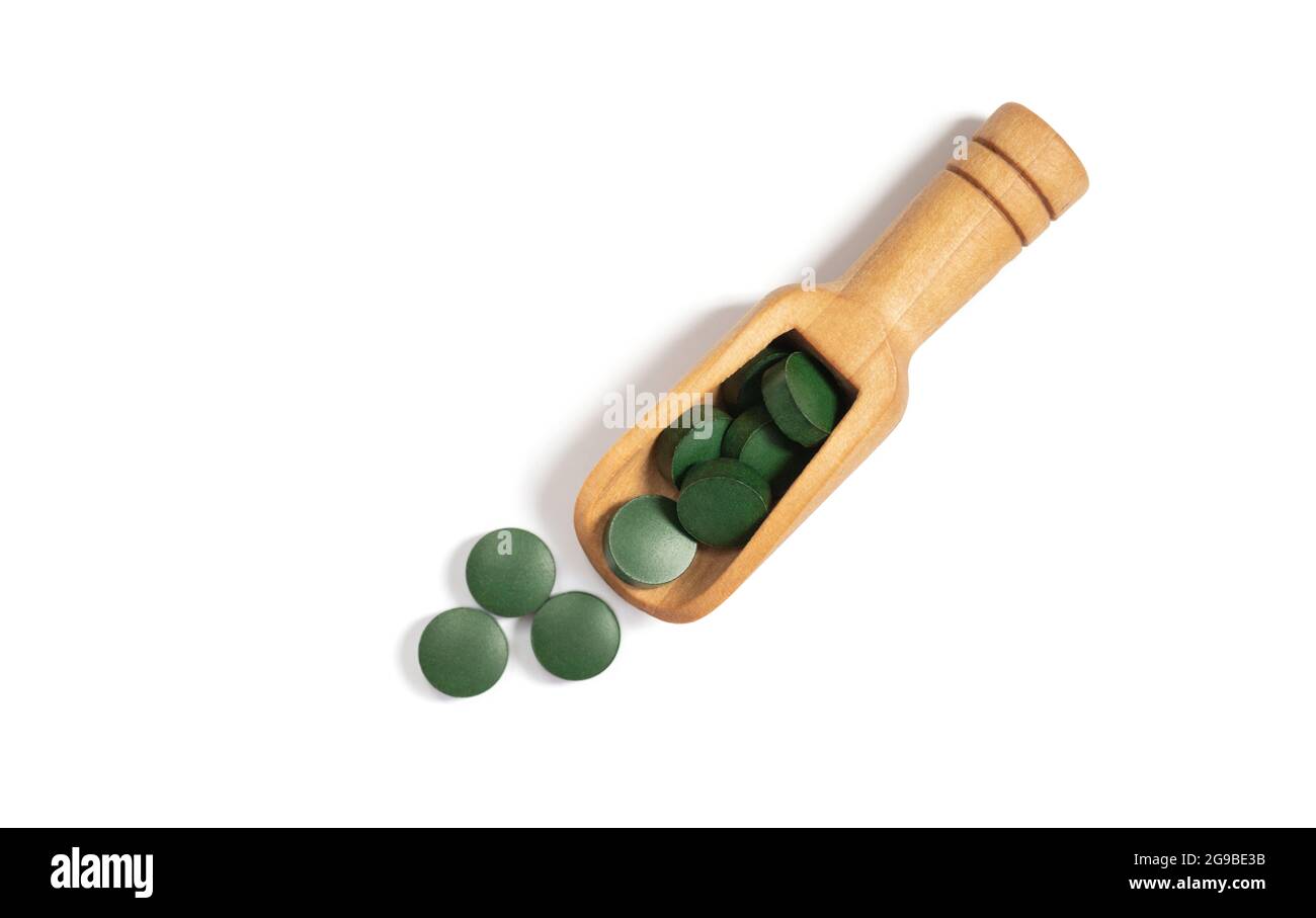 Pilules vertes de spiruline dans une cuillère en bois isolée sur un fond blanc. Comprimés de Chlorella. Vue de dessus, plan d'appartement. Banque D'Images
