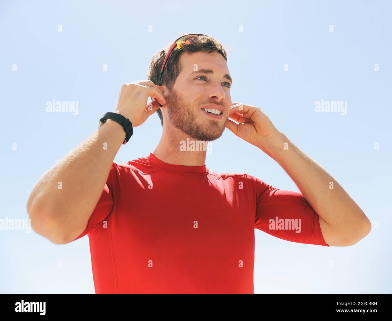 Jeune homme qui met un casque sans fil bluetooth connecté à des écouteurs SmartWatch pour courir en plein air. Bonne personne active qui porte des écouteurs pour Banque D'Images