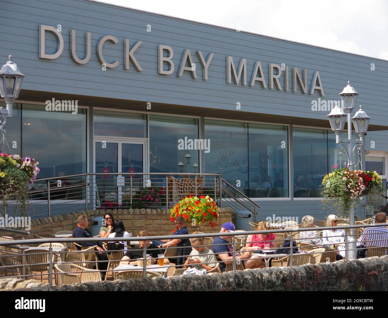 Les gens profitent du soleil et s'assoir sur la terrasse du restaurant de Duck Bay Marina, qui donne sur le Loch Lomond. Banque D'Images